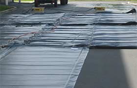 Concrete curing blankets laid on a roadway for thermal protection and consistent curing of concrete.