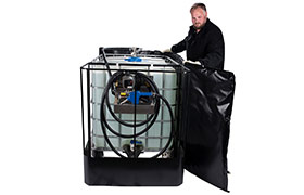 Worker wrapping a DEF fluid tank with a heater blanket for temperature regulation in a warehouse setting.