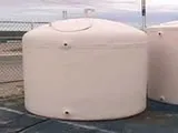 A white cylindrical fiberglass water storage tank with connection points at the bottom and top.