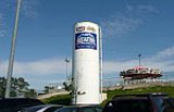 Tall vertical white steel water tank with a visible logo, installed in an outdoor area near a parking lot.