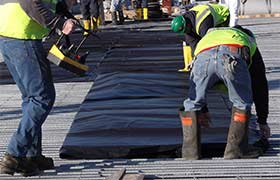 Workers installing concrete curing blankets on a construction site to maintain temperature and moisture for curing.