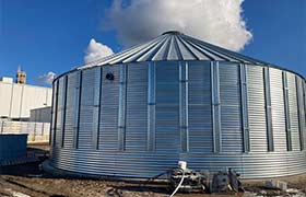 Corrugated steel water storage tank installed outdoors, designed for large-capacity water storage.