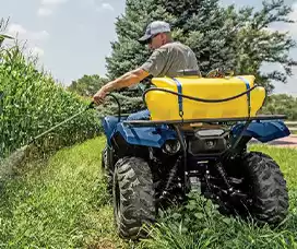 ATV sprayer with a yellow tank, spraying crops in a field for targeted and efficient liquid application.